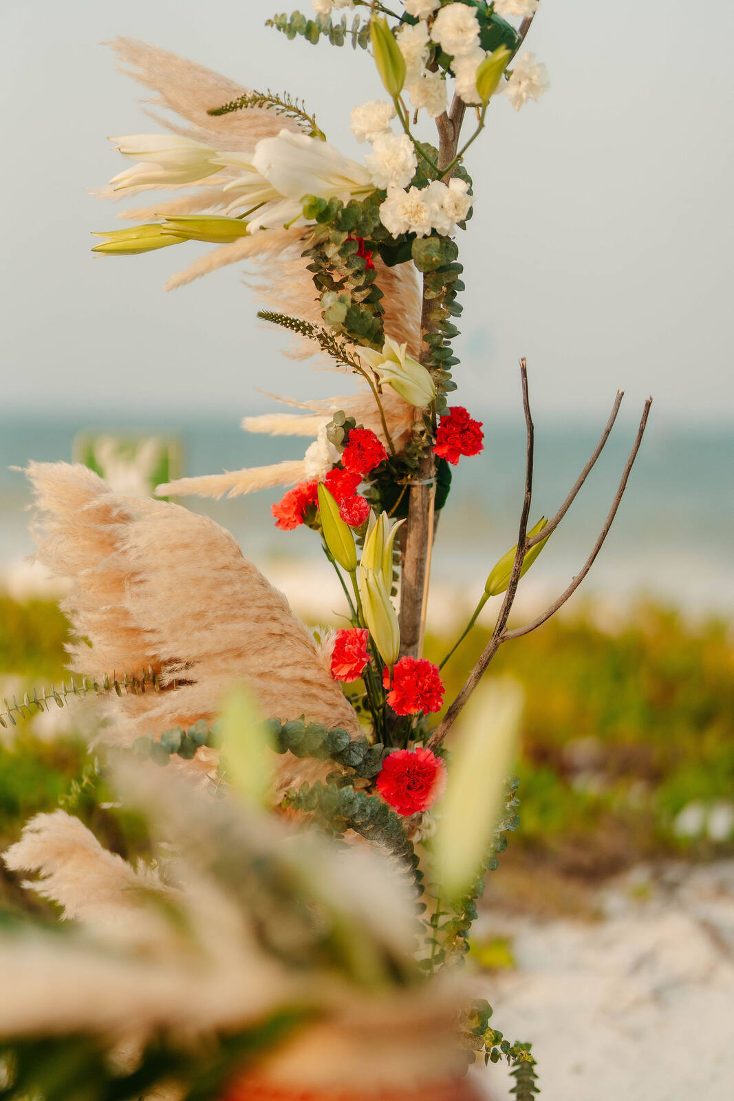 A ceremony floral installation with pampas grass, carnations and eucalyptus by the shore
