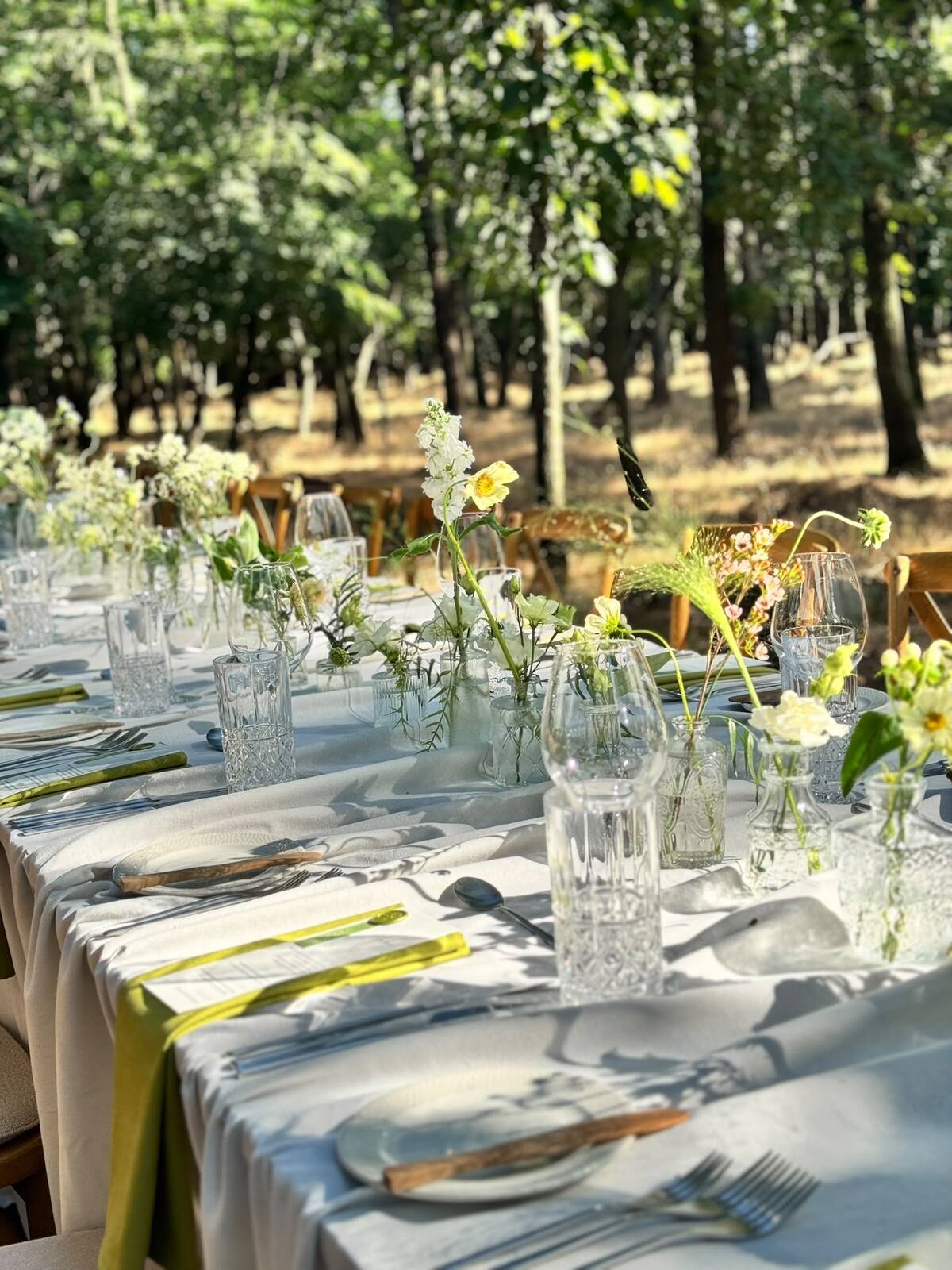 A tablescape styled with linen, wildflowers and vintage glassware among the trees